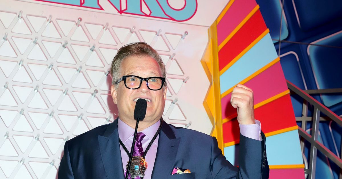 Drew Carey in a dark blue suits posing with a microphone 