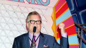 Drew Carey in a dark blue suits posing with a microphone