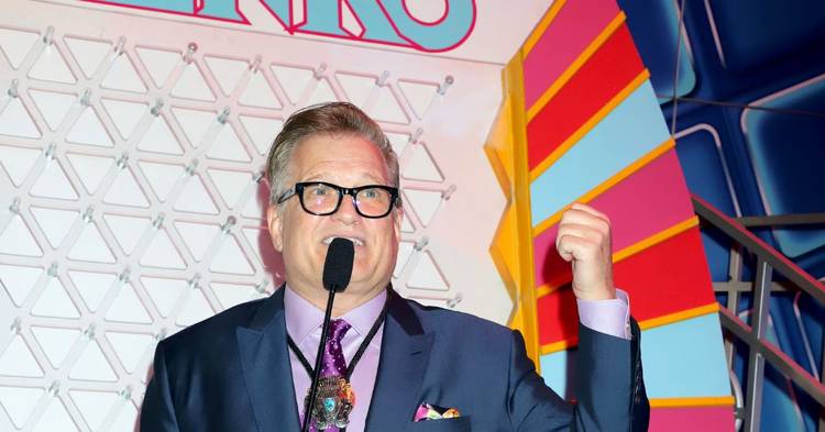 Drew Carey in a dark blue suits posing with a microphone