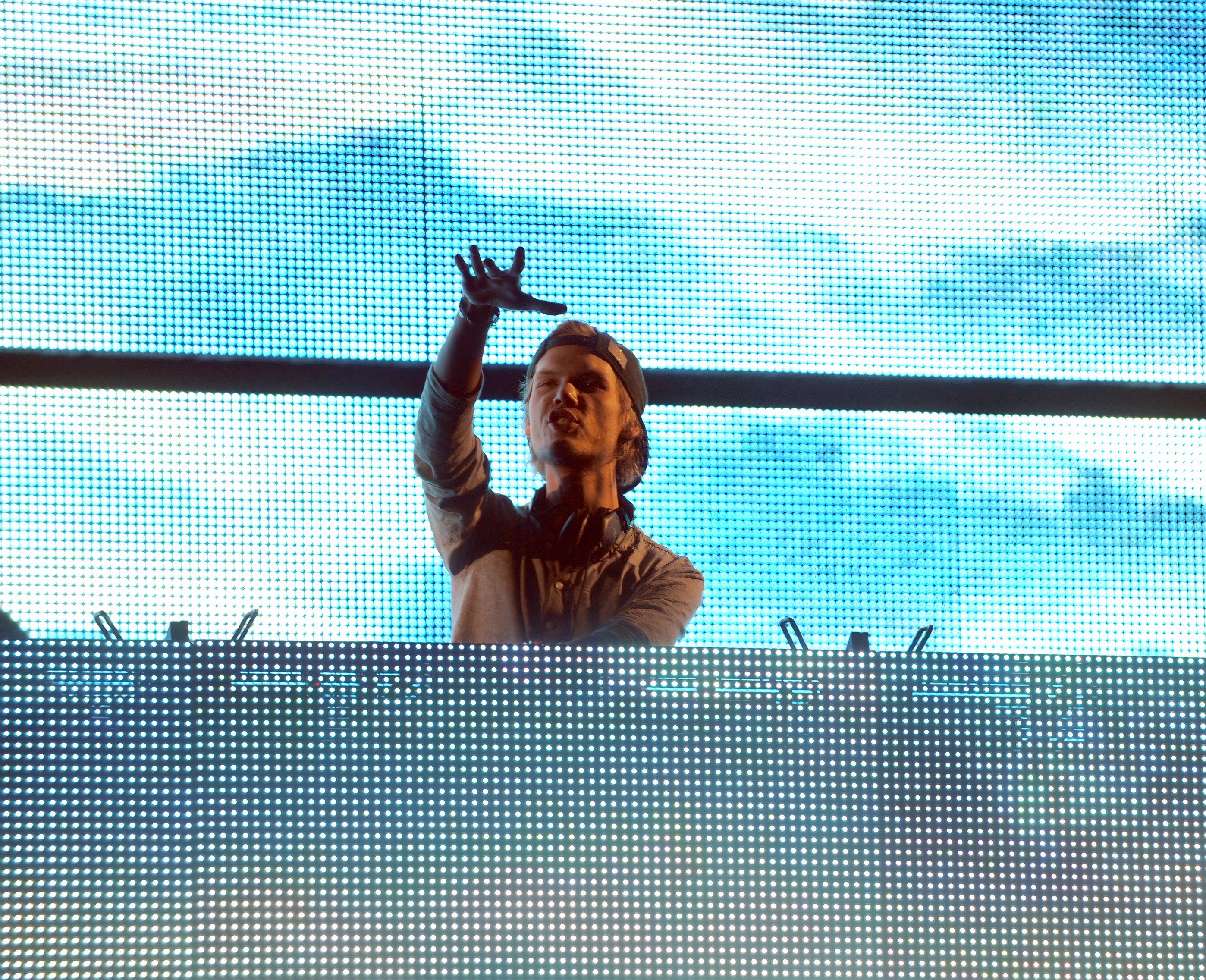 dj avicii performs on a blue lit stage