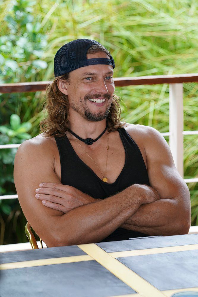 a man in a backwards cap and black tank sits at a table